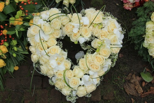 Funeral flower heart with white roses, lisianthus and orchids sitting on the ground.