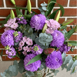 Purple flowers in a glass vase against a brick wall.