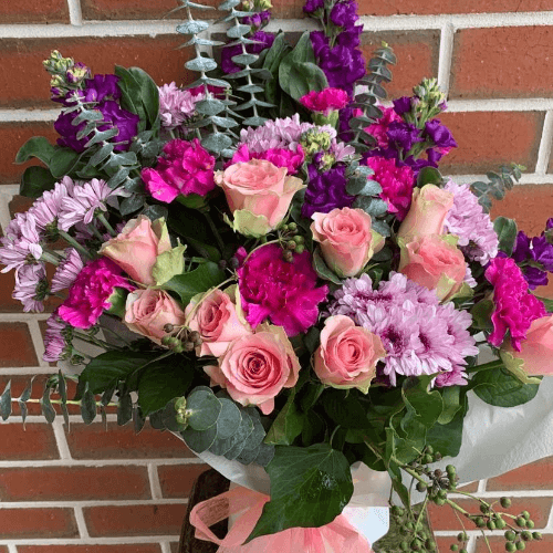 Pink roses, carnations, chrysanthemums and purple stock flower bouquet wrapped in white paper and pink ribbon.