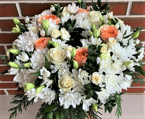 flower wreath of white and orange flowers sitting on a stand.