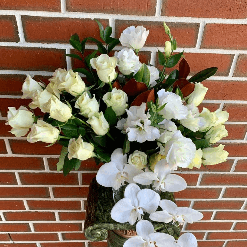 White roses, lisianthus and phalaenopsis orchids arranged in a glass vase.