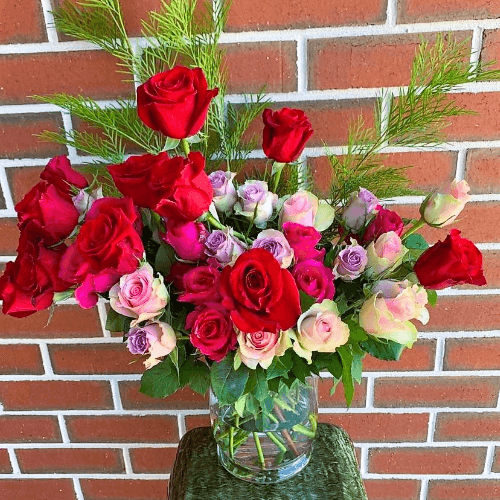 Red, pink and purple roses arranged in a glass vase.
