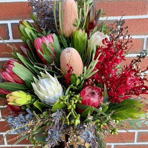 Red, green and white native flowers arranged in a gold ceramic pot.