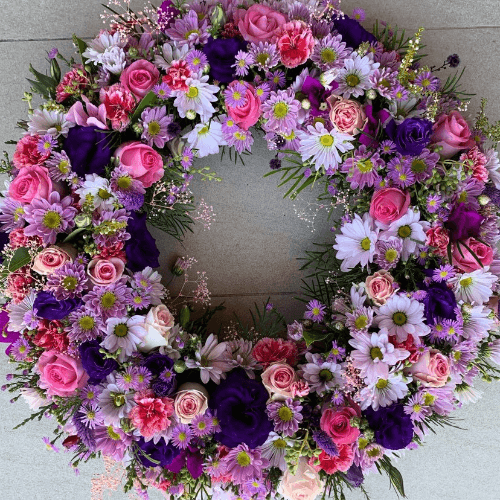 Pink and purple funeral flower wreath sitting on the floor.