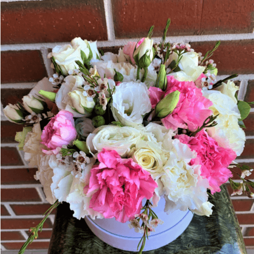 Pink and white flowers arranged in a white hatbox.