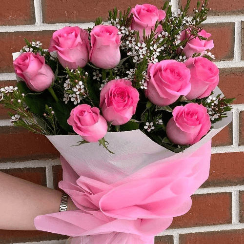 Pink roses and wax flowers wrapped together in white and pink paper.