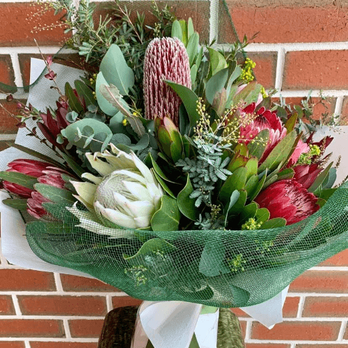 Assortment of native flowers wrapped in white paper and green net.