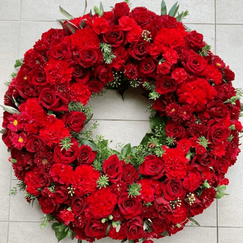 Red roses, carnations, celosia and aster flower wreath sitting on the ground