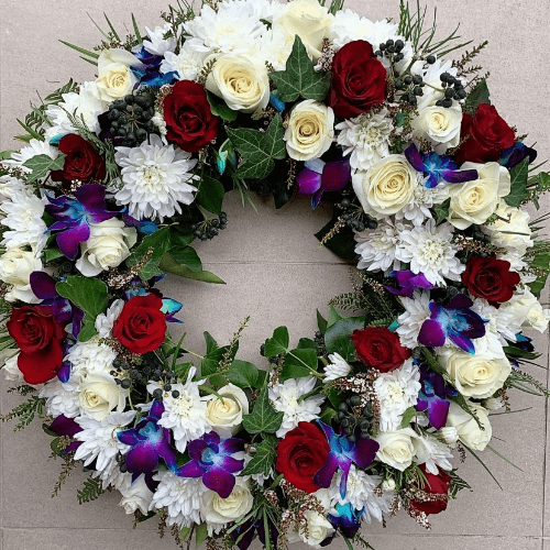 White, red and blue funeral wreath sitting on the ground.
