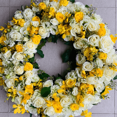 White and Yellow funeral flower wreath sitting on the floor.