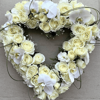 White roses and orchids funeral heart sitting on the ground.