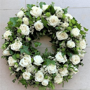White roses funeral wreath sitting on the ground.