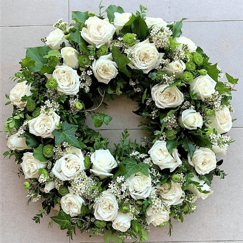 White roses funeral wreath sitting on the ground.