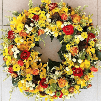 Yellow and orange funeral flower wreath sitting on the ground.