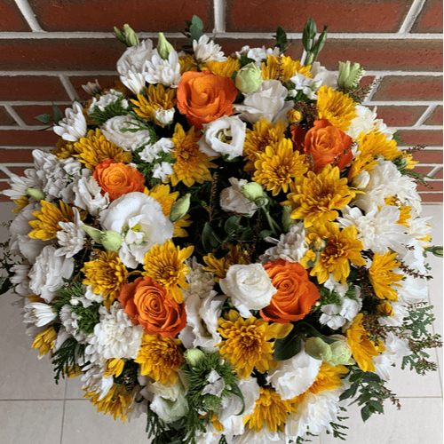 flower wreath of white and orange flowers sitting on a stand.