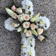 Funeral cross with white and peach flowers sitting on the ground.