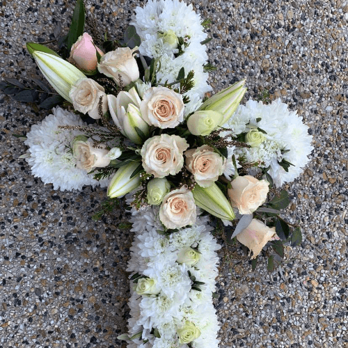 Funeral cross with white and peach flowers sitting on the floor.