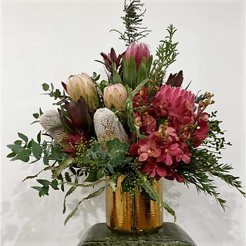 Red, green and white native flowers arranged in a gold ceramic pot.