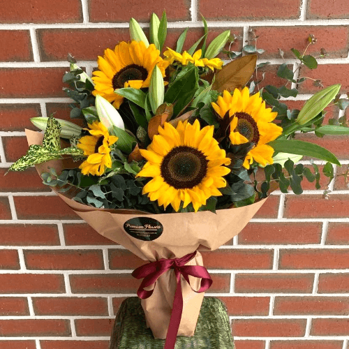Bunch of wrapped sunflowers and oriental lilies sitting on a stand.